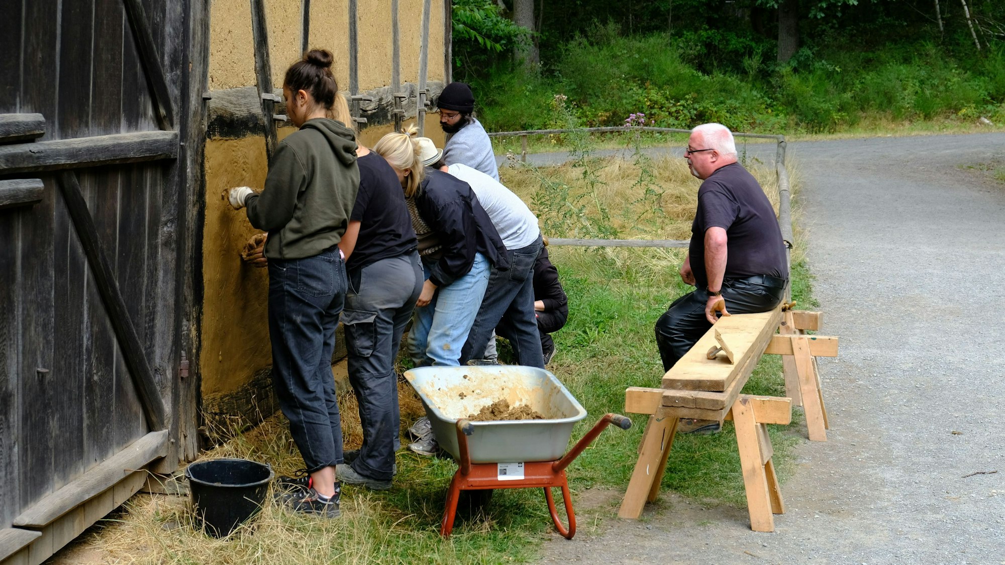 Mehrere junge Leute tragen Lehm als Putz eines Fachwerkhauses auf.
