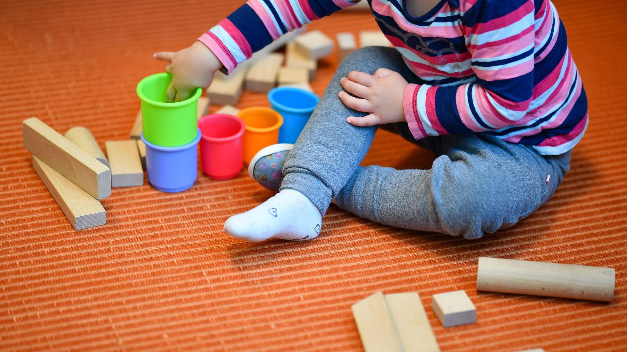 Ein Mädchen spielt in einer Kita mit bunten Bechern und Bauklötzen