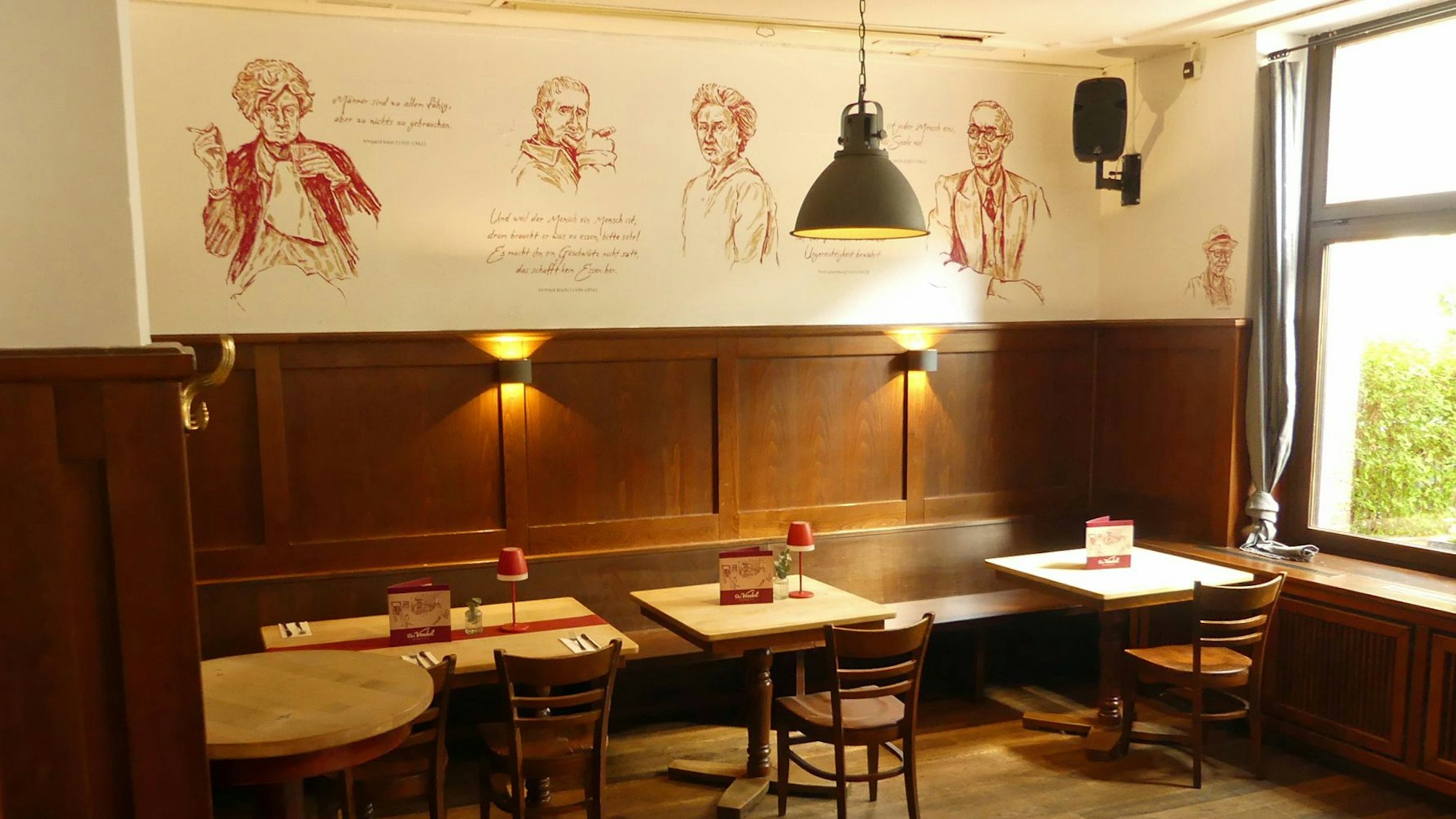 Holztische und Stühle stehen an einer Wand mit roten Gemälden.