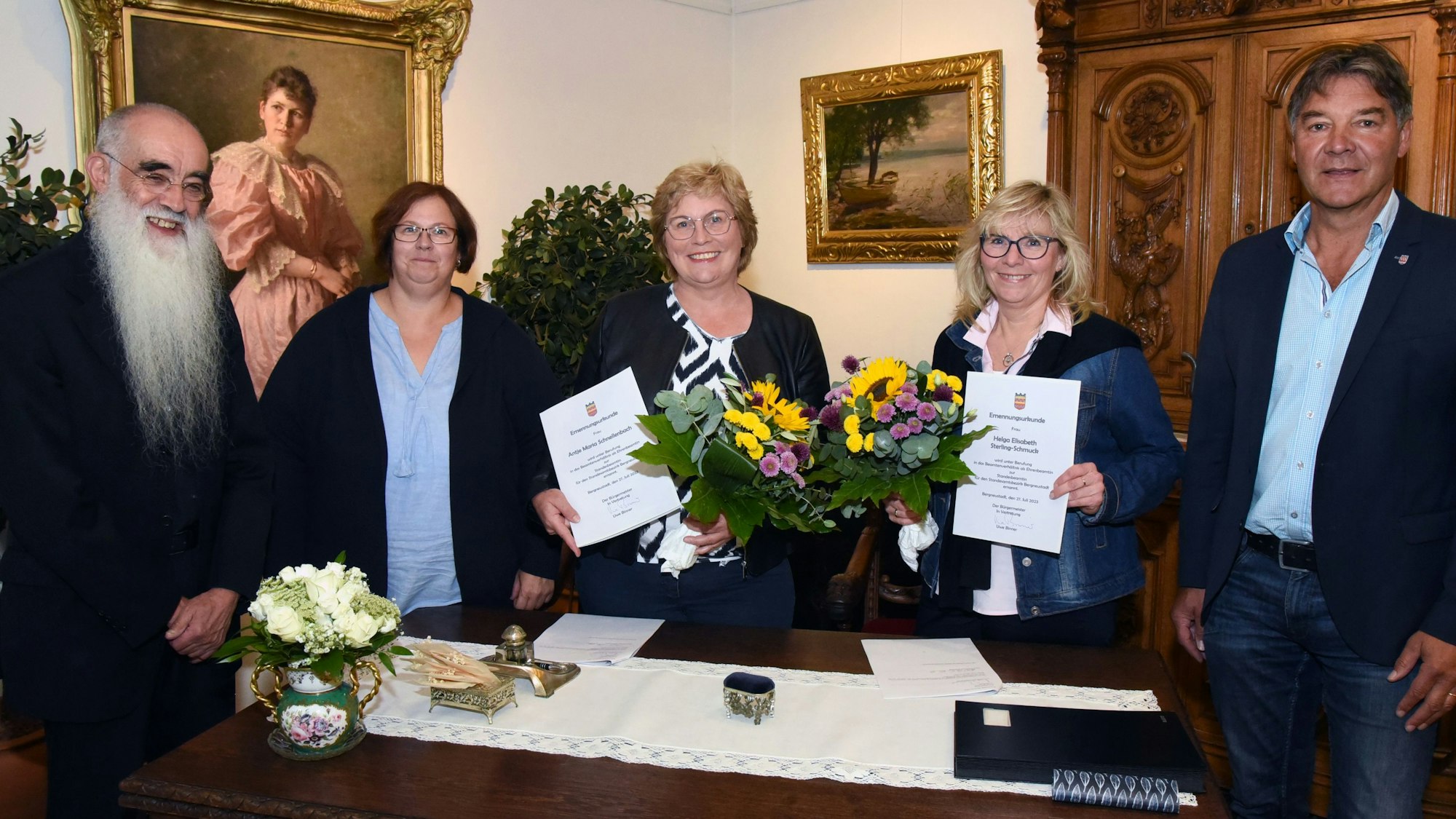 Mehrere Personen stehen in einem Trauzimmer. Zwei Frauen halten Zertifikate in den Händen.
