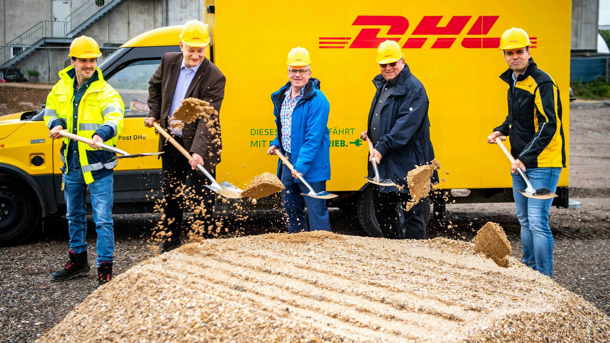 Das Foto zeigt fünf Männer mit Spaten vor einem DHL-Fahrzeug.