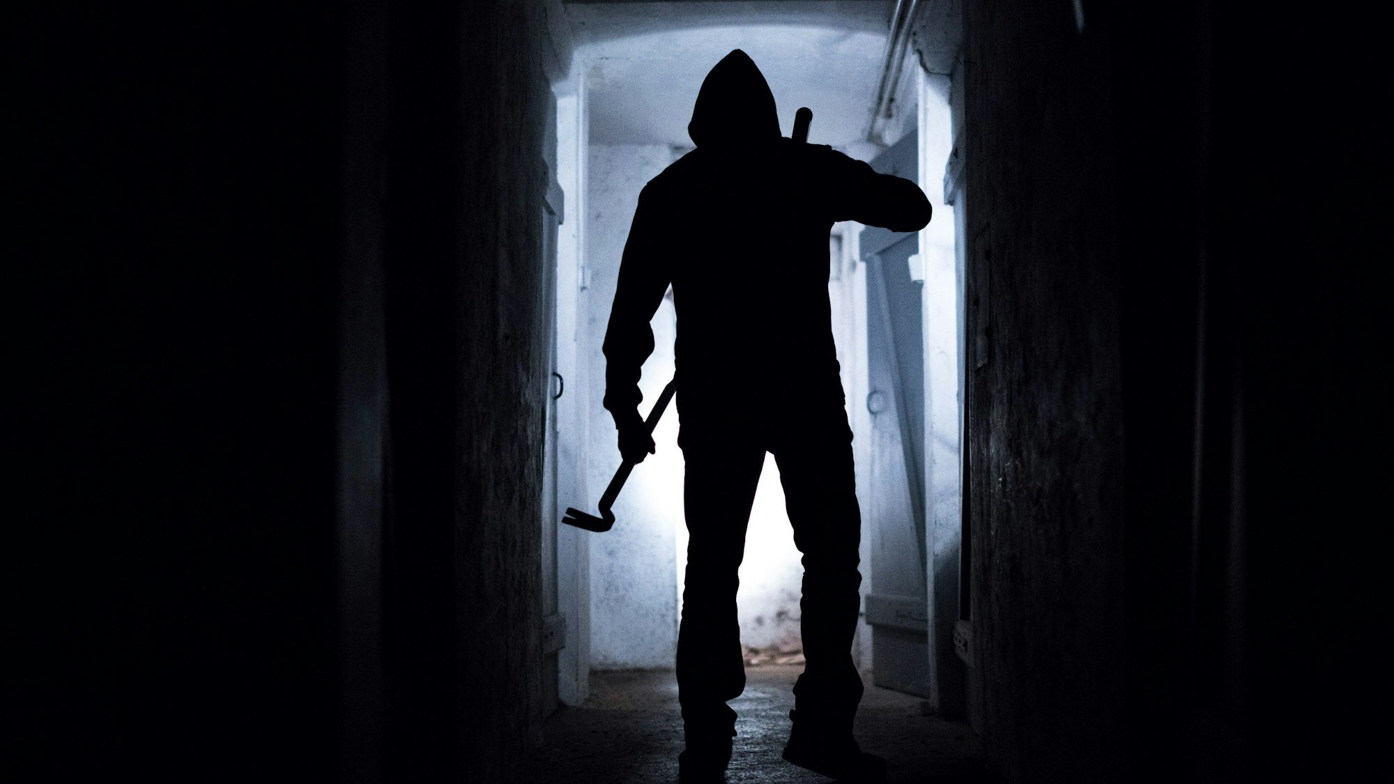 Eine Person mit einer Brechstange steht in einem dunklen Gang.(Symbolbild)