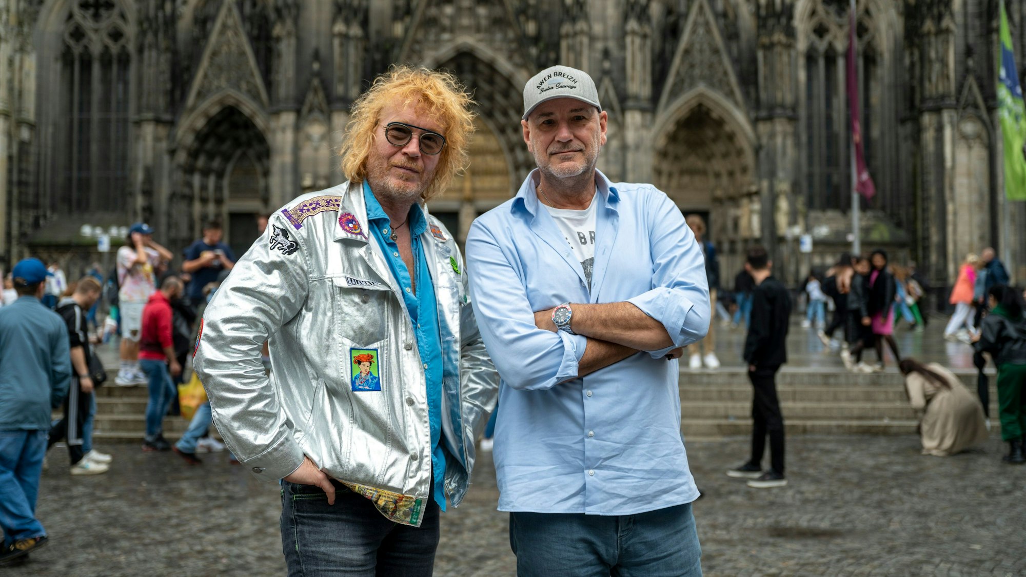 Christof Stein-Schneider in silbener Jacke und Kai Wingenfelder im blauen Hemd und Kappe, posieren vor dem Kölner Dom.
