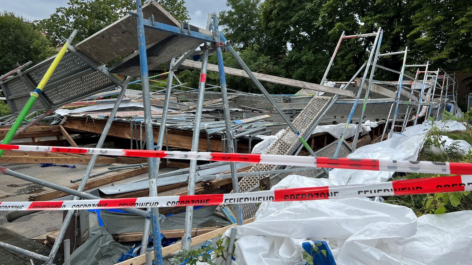Hinter einem rot-weißen Absperrband der Polizei sind nur Trümmer des Baugerüsts und Holzteile zu sehen, die übereinander liegen.
