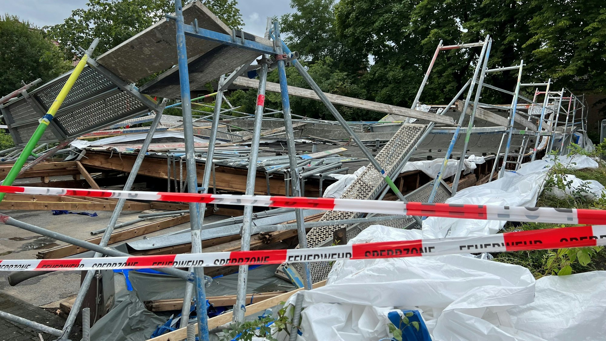 Hinter einem rot-weißen Absperrband der Polizei sind nur Trümmer des Baugerüsts und Holzteile zu sehen, die übereinander liegen.