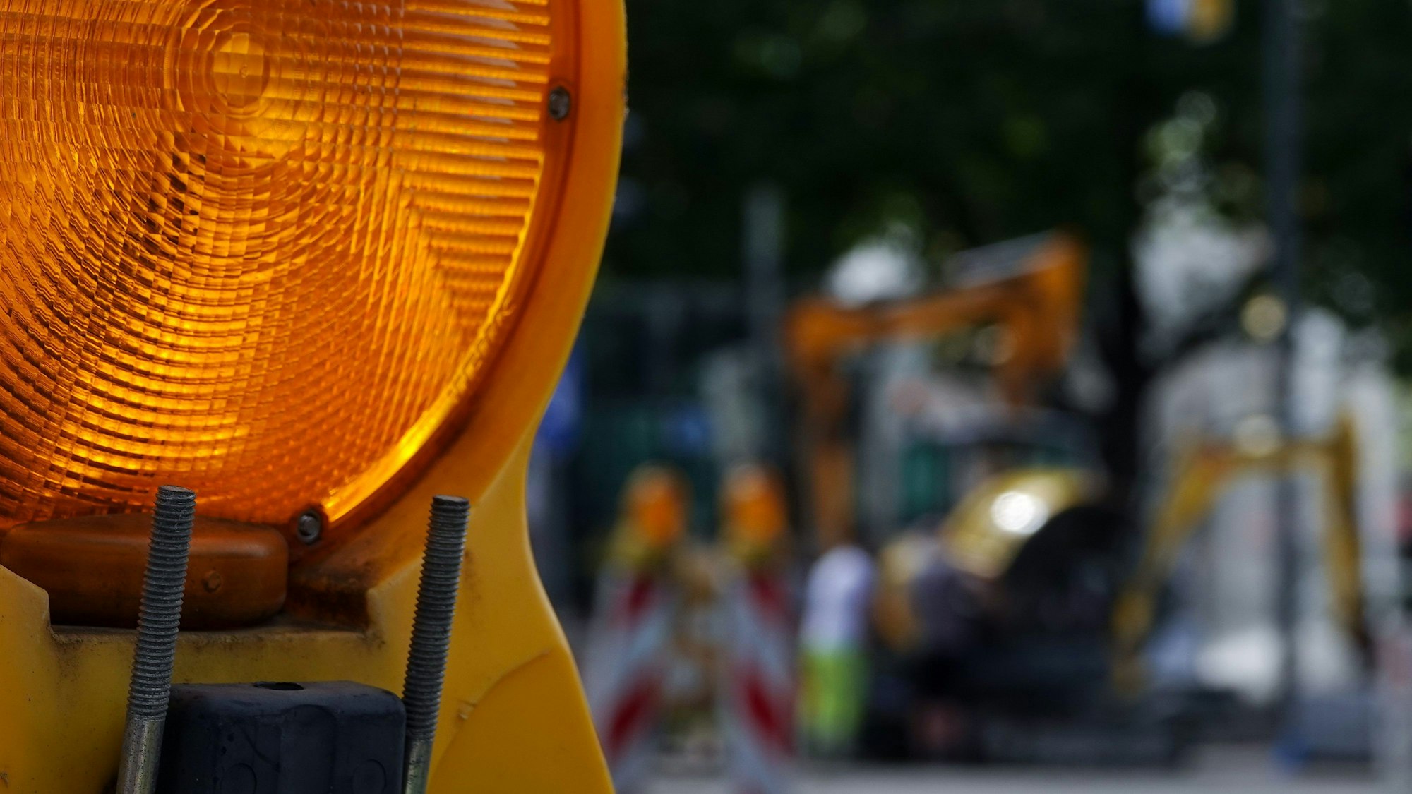 Ein Baustellenreflektor im Vordergrund. Im Hintergrund ist verschwommen ein Bagger und weitere Baustellenhinweise zu sehen.