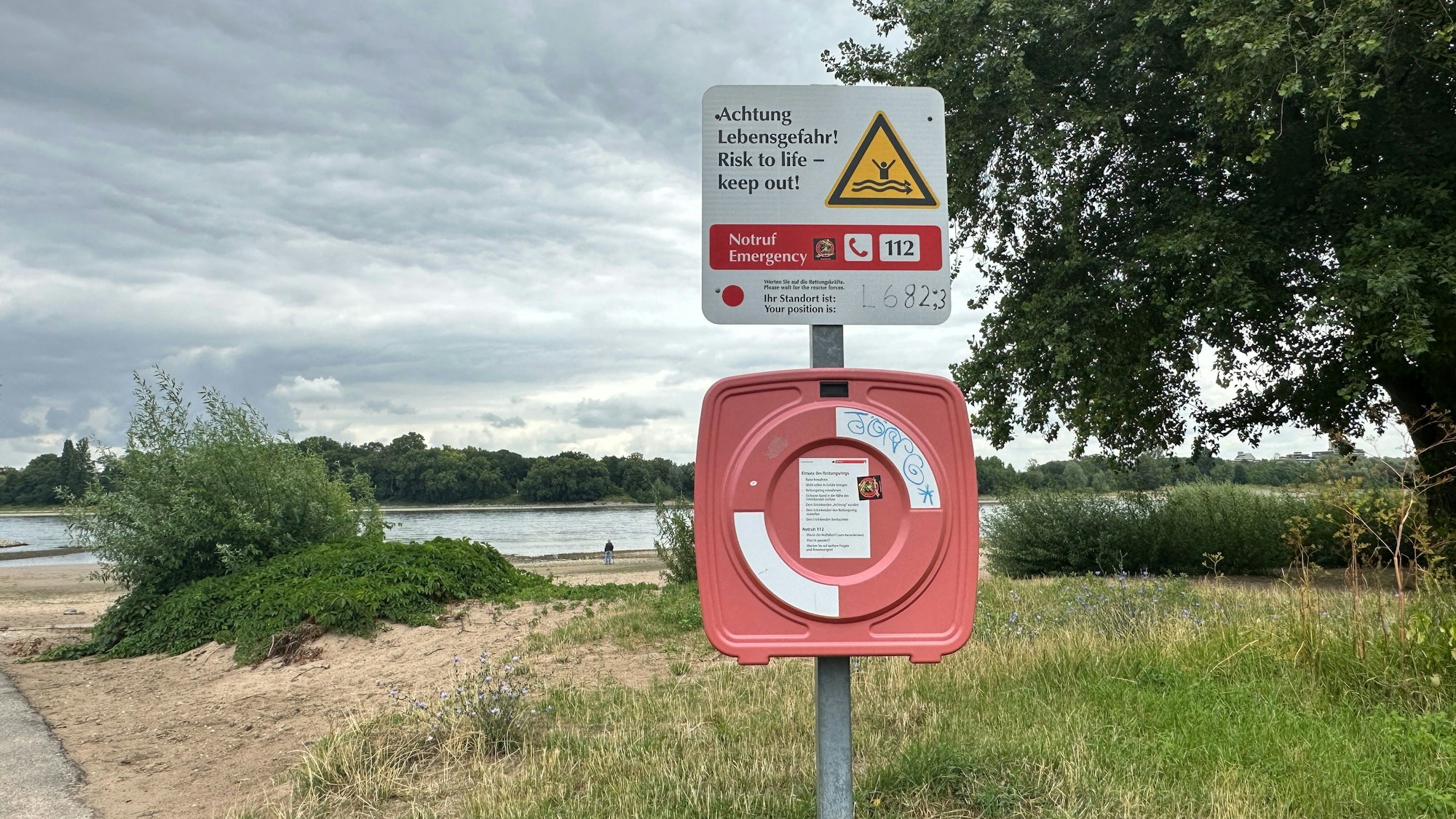 Am Rhein steht ein Mast mit einer Box, in der der Rettungsring steckt.