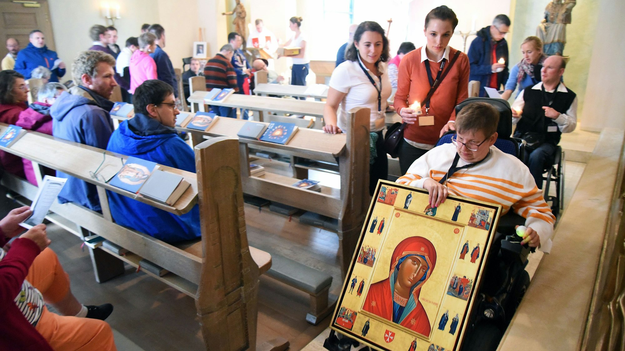 Menschen, teilweise im Rollstuhl, in einer Kapelle. Eine Frau hält ein Marienbild in der Hand.