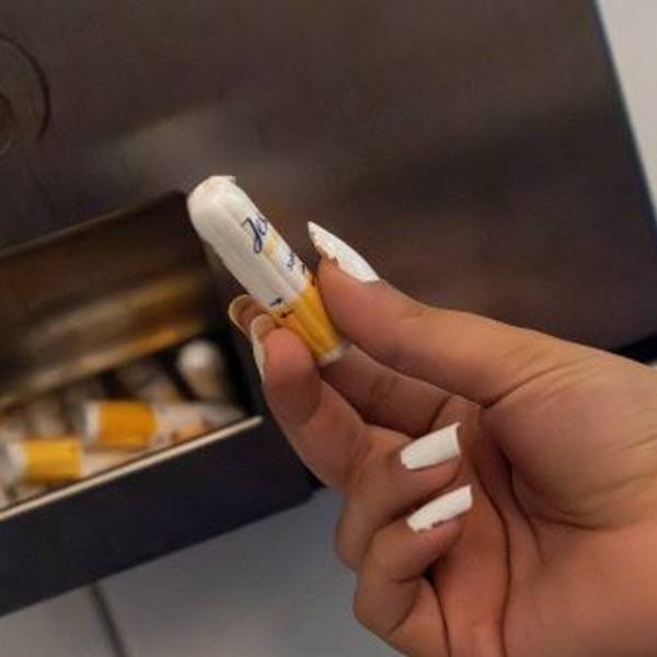 Eine Schülerin hält einen Menstruationsartikel vor einem Menstruationsartikel-Spender.