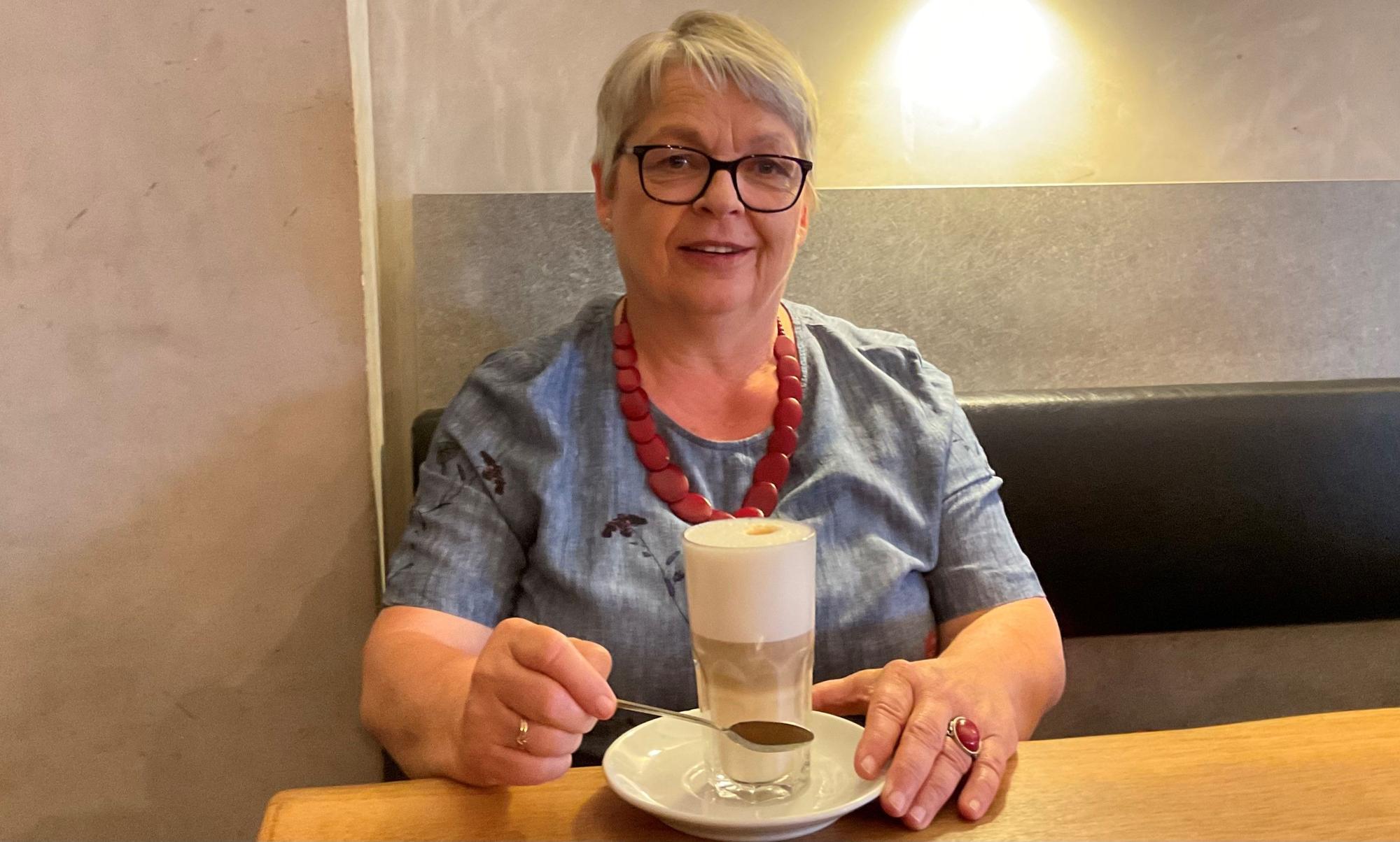Grauhaarige Frau im Café mit Latte Macchiato