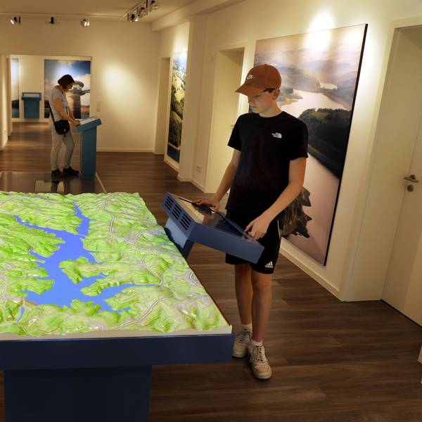 Menschen stehen an Stationen und einem großen Relief der interaktiven Ausstellung „Wasser verbindet“ im Auqalon-Forum an der Großen Dhünn-Talsperre.