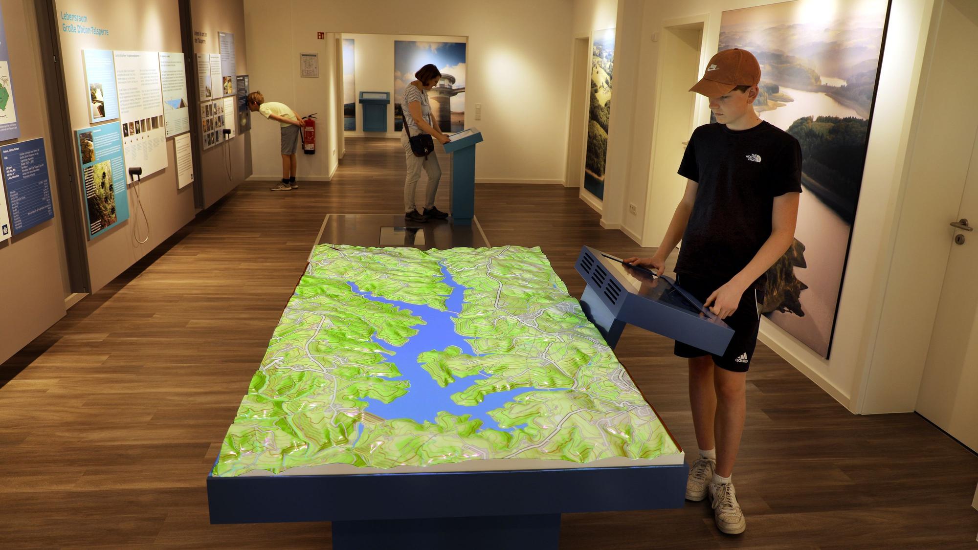 Menschen stehen an Stationen und einem großen Relief der interaktiven Ausstellung „Wasser verbindet“ im Auqalon-Forum an der Großen Dhünn-Talsperre.
