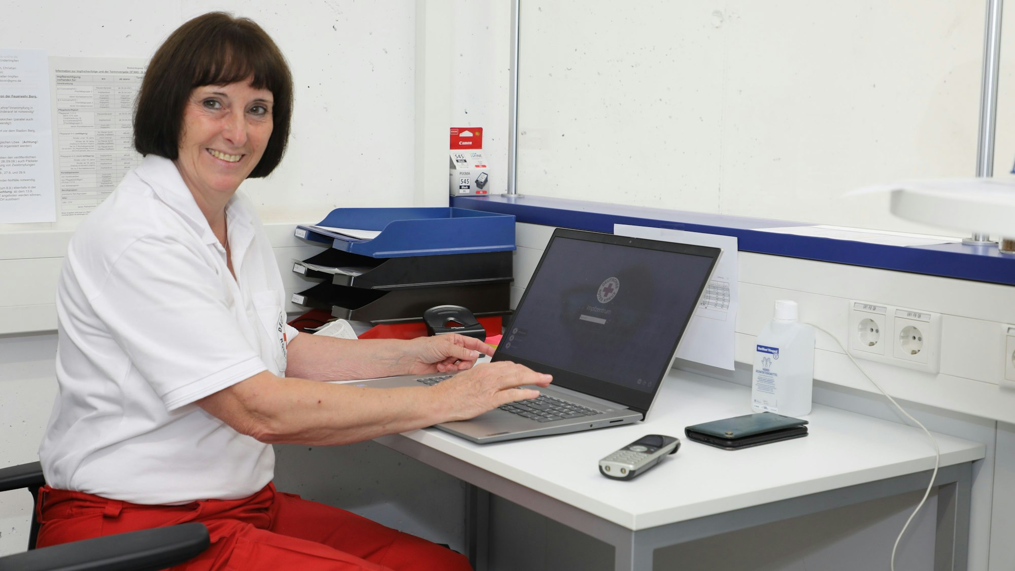 DRK-Kreisvorsitzende Ingeborg Schmidt sitzt mit einem Laptop an einem Tisch im Impfzentrum des Rheinisch-Bergischen Kreises.