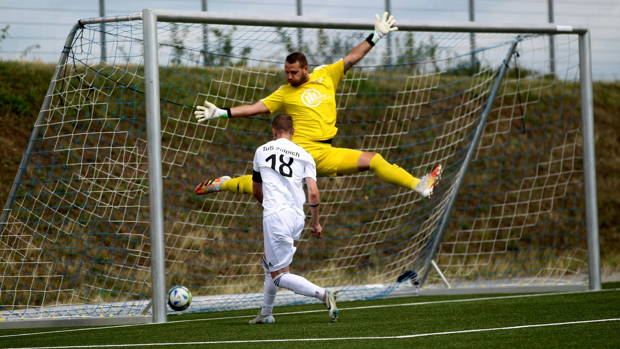 Der D-H-O-Torhüter im knallgelben Dress springt, Arme und Beine ausgebreitet hoch, Zülpichs Stürmer trifft aber flach ins Eck.