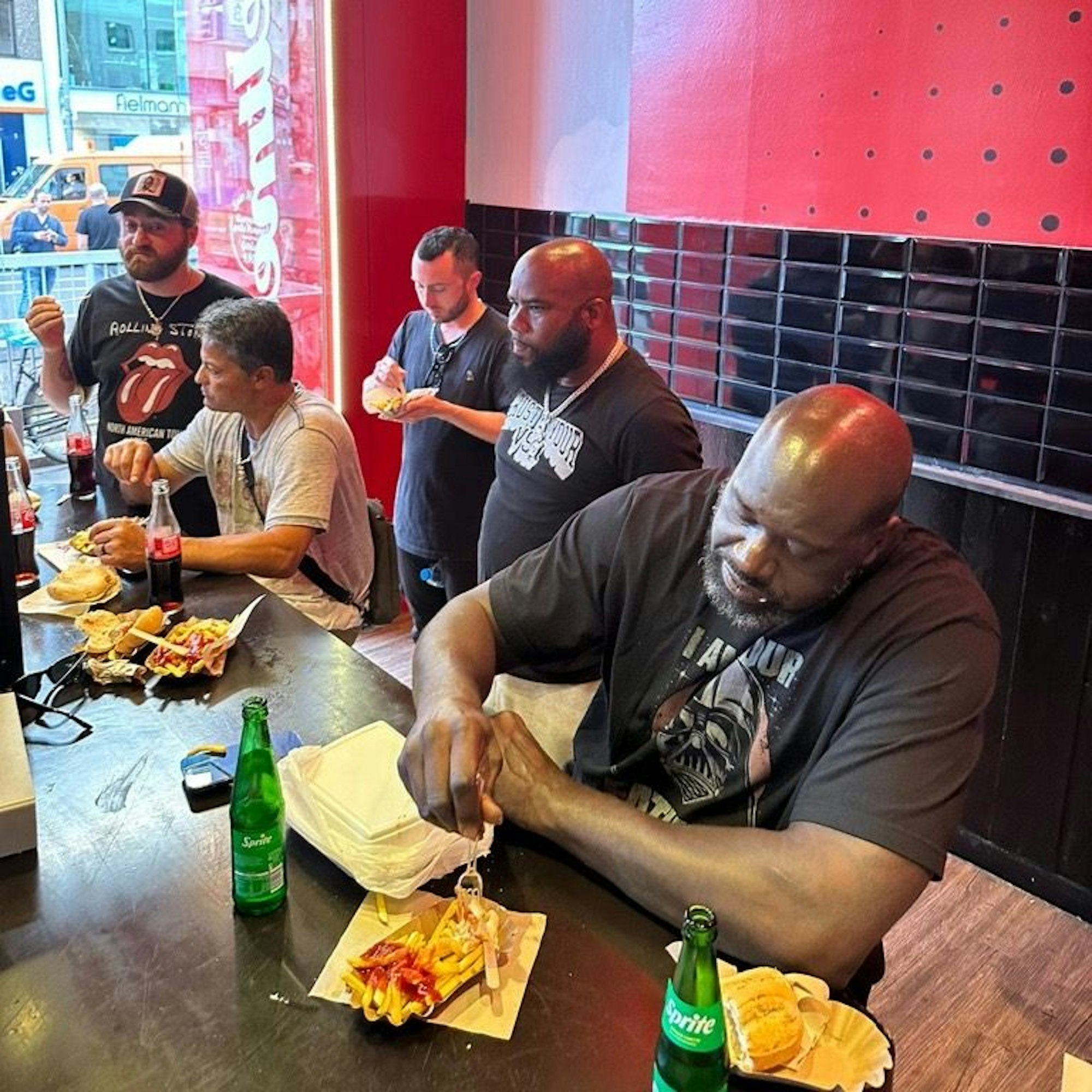 Shaquille O'Neal isst am 28. Juli 2023 im Weltmeister am Kölner Ebertplatz eine Pommes mit Wurst.