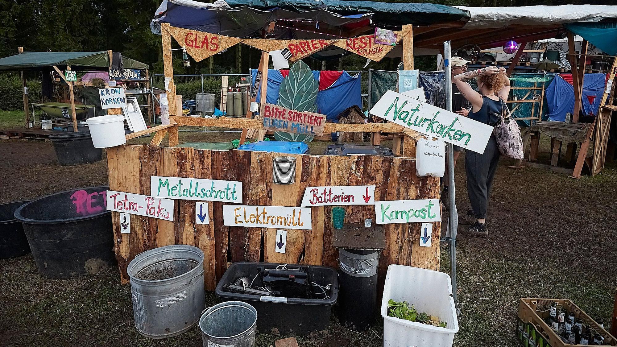 Das Bild zeigt eine aus Holz gestaltete Mülltrennungsstation bei einem Festival.