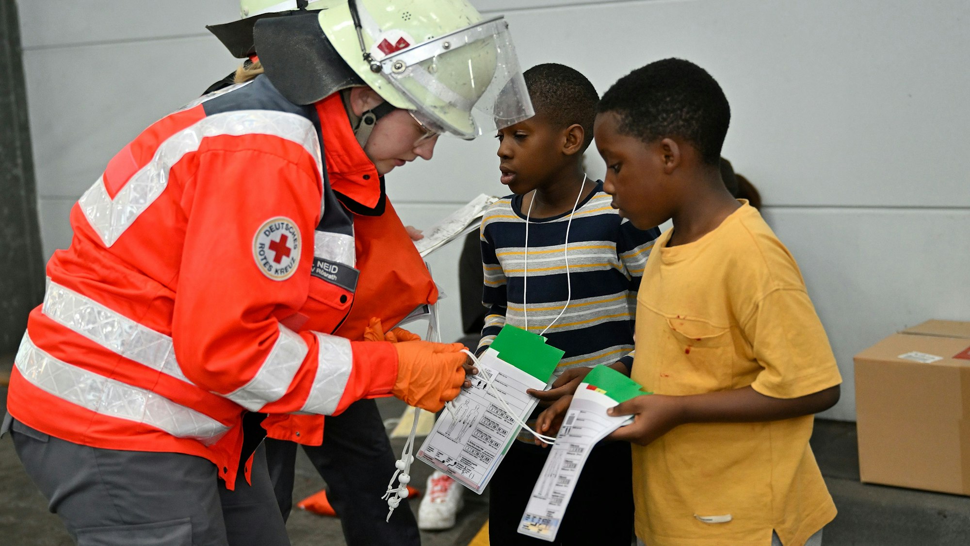 Eine DRK-Einsatzkraft gibt zwei Kindern grüne Vereltztenanghängekarten.