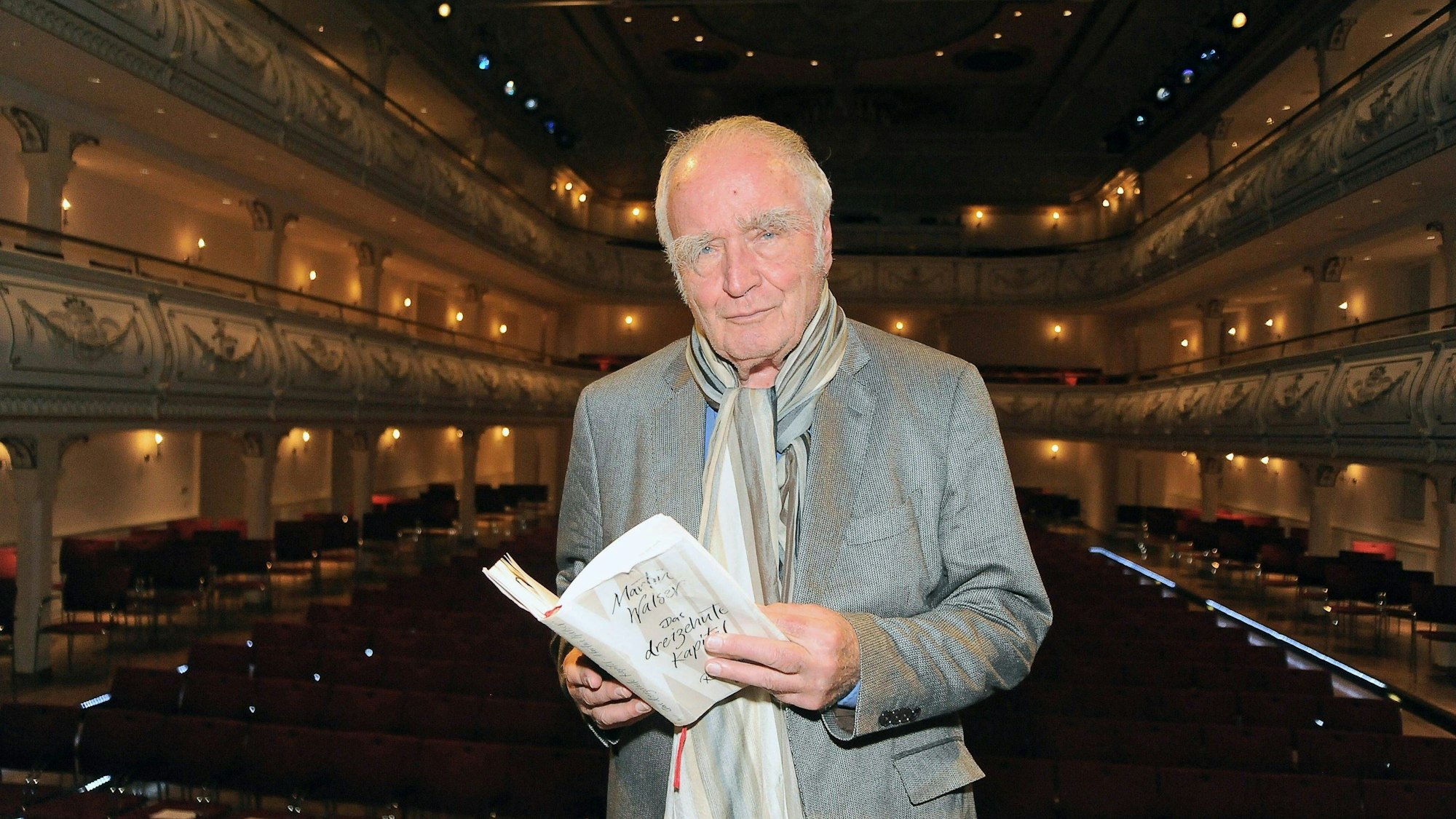 Martin Walser hält im Erfurter Kaisersaal ein aufgeschlagenes Buch in den Händen und schaut in die Kamera.
