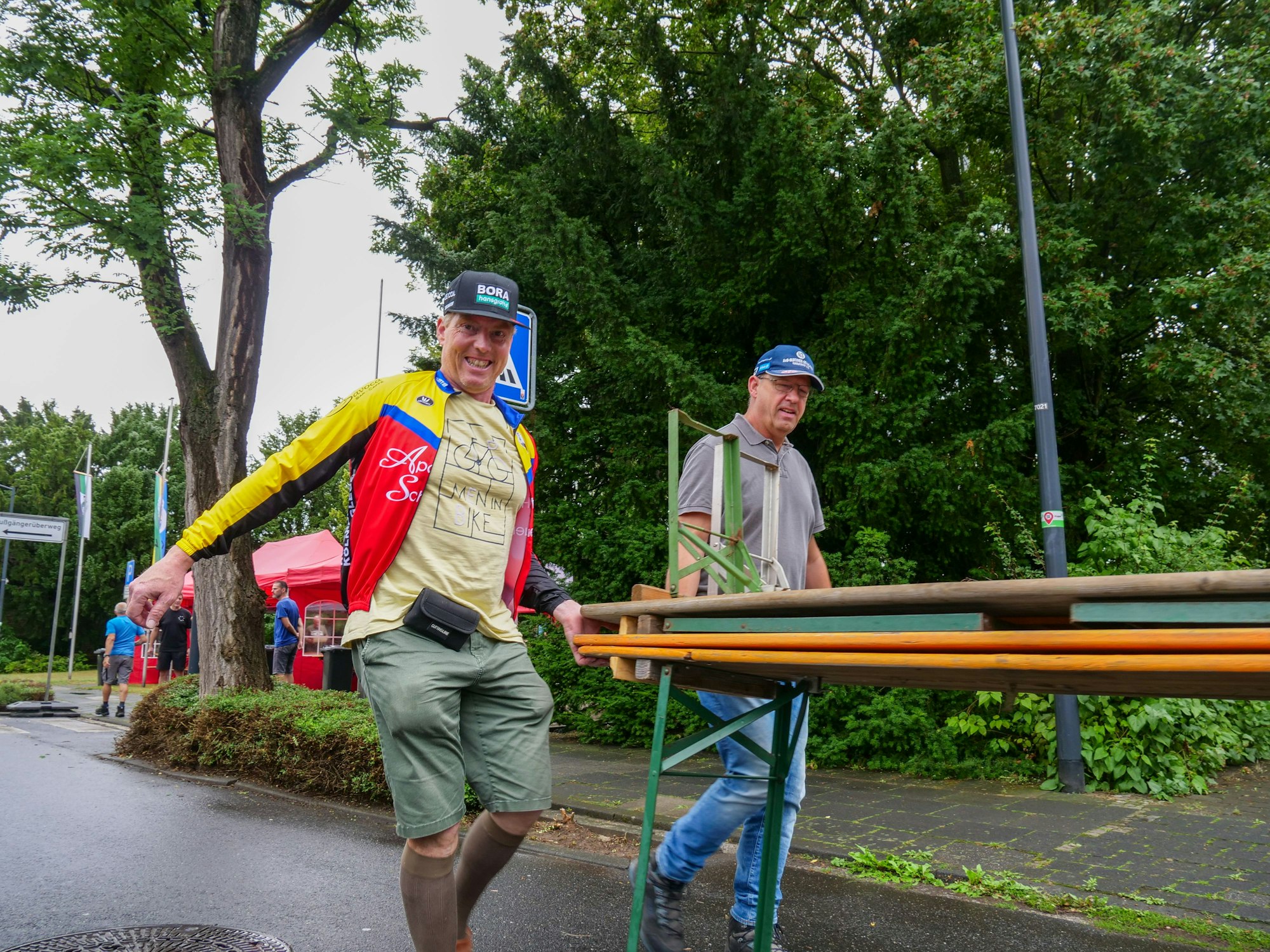 Das Bild zeigt zwei Männer, die Biertische tragen.