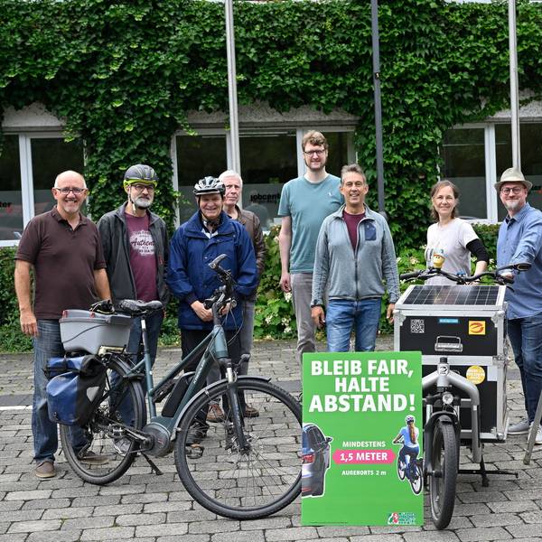 Die Beteiligten stehen um ein Abstands-Schild herum.