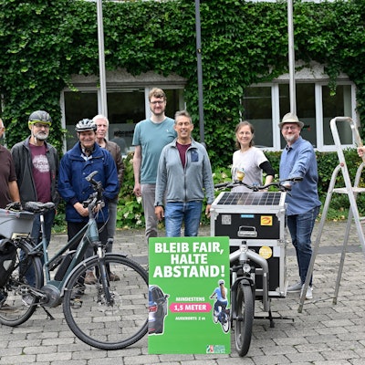 Die Beteiligten stehen um ein Abstands-Schild herum.