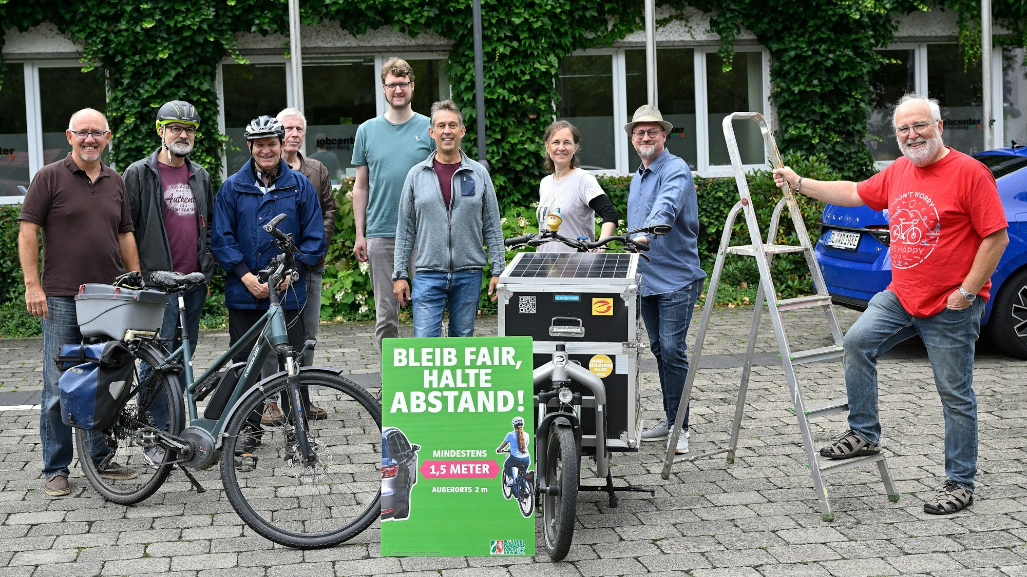 Die Beteiligten stehen um ein Abstands-Schild herum.