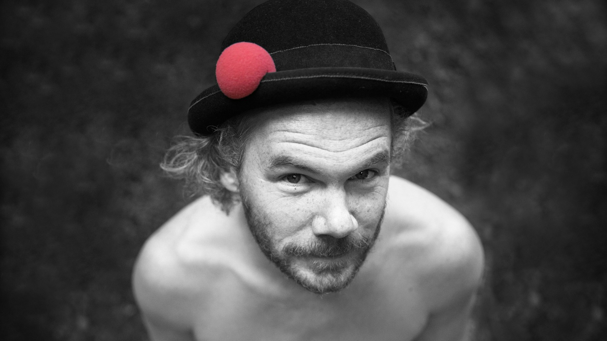 Das schwarz-weiß Foto zeigt den oberkörperfreien Musik-Kabarrettisten Nisse Barfuss. Er trägt einen schwarzen Hut mit einer roten Clownsnase daran.