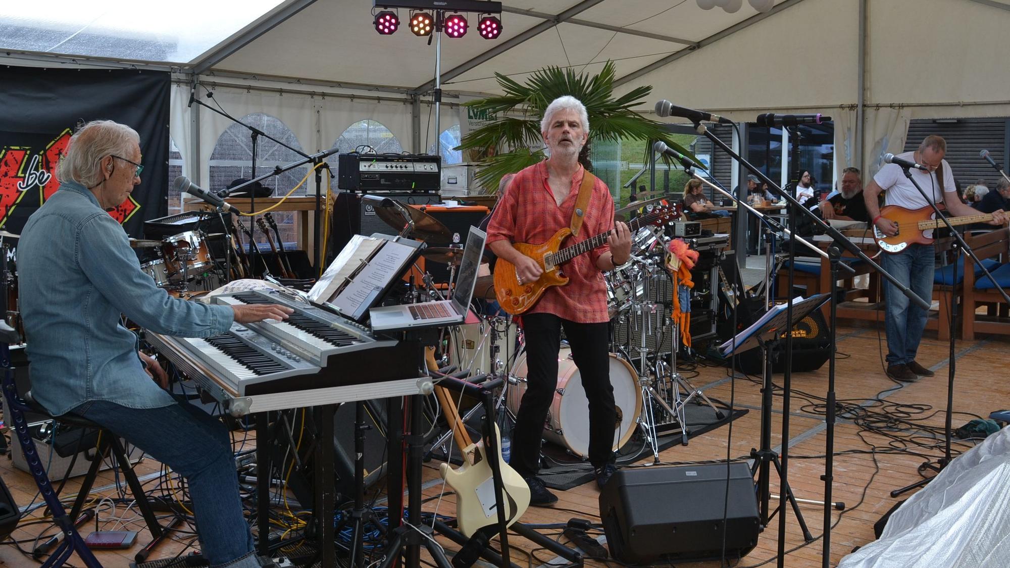 Mitglieder der Band Into Deep spielen auf einer Bühne E-Piano, Bass und Gitarre.