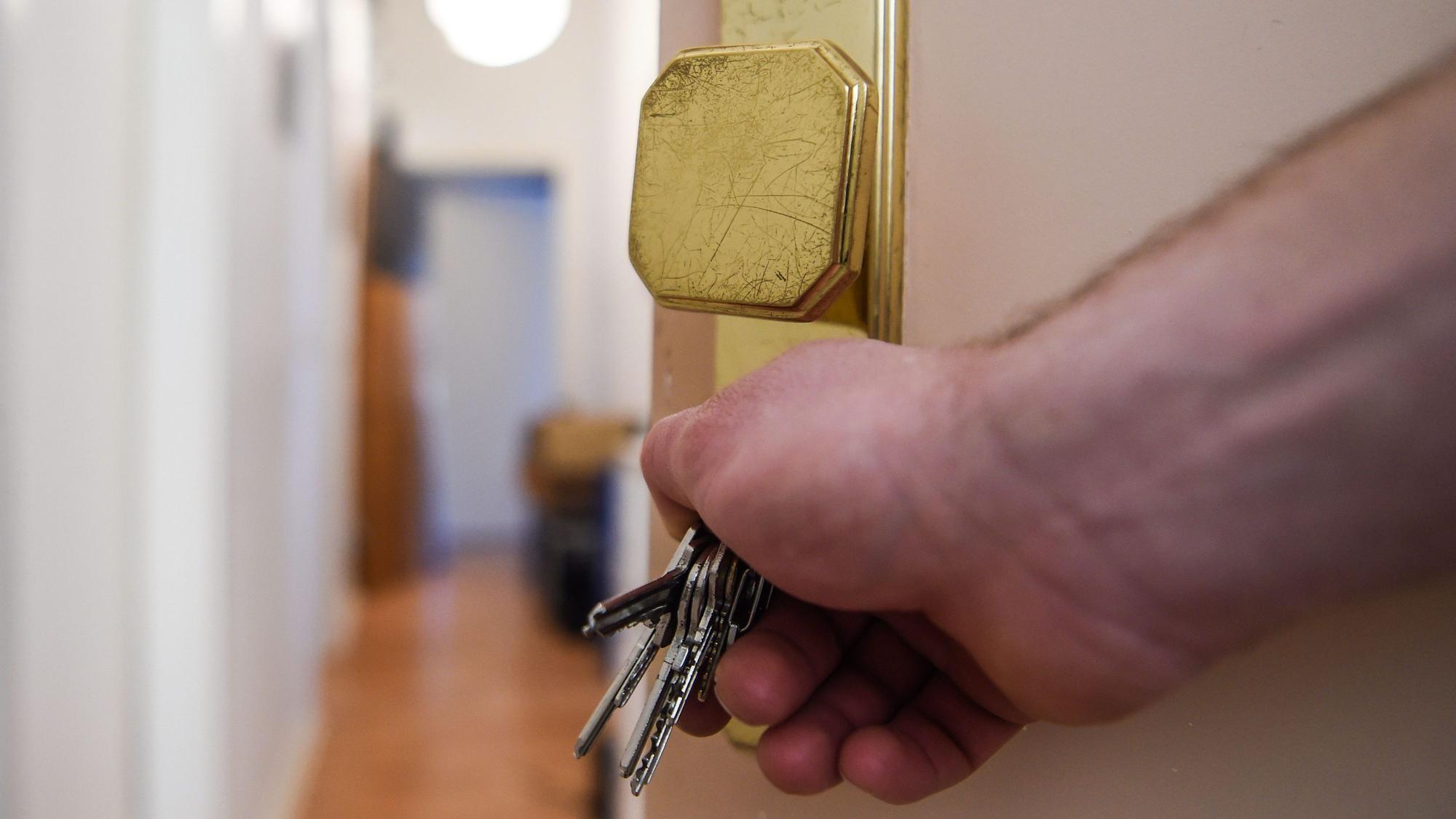 Das Bild zeigt einen Mann, der mit einem Schlüssel eine Wohnungstür aufschließt.