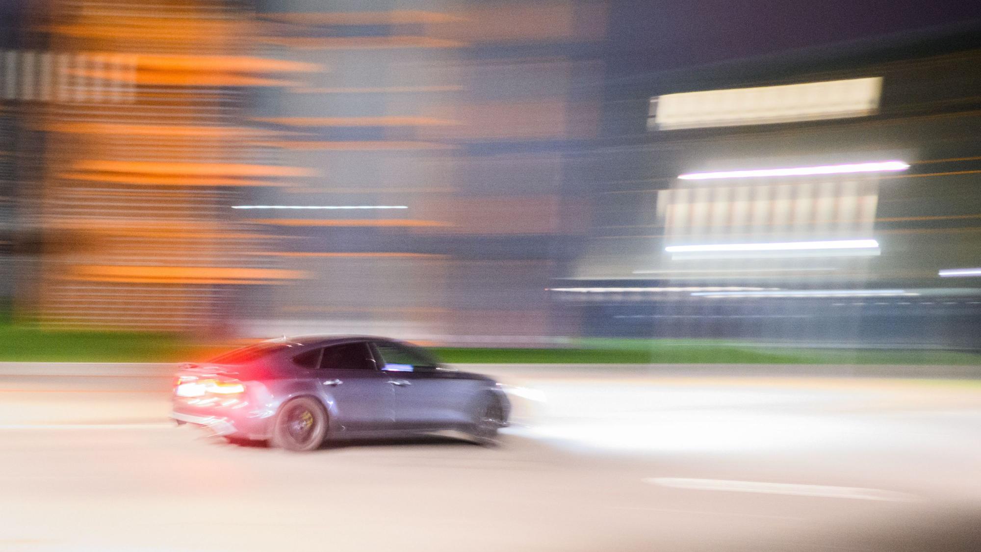 Ein getuntes Auto fährt scnell durch die nächtlich beleuchtete Straße.