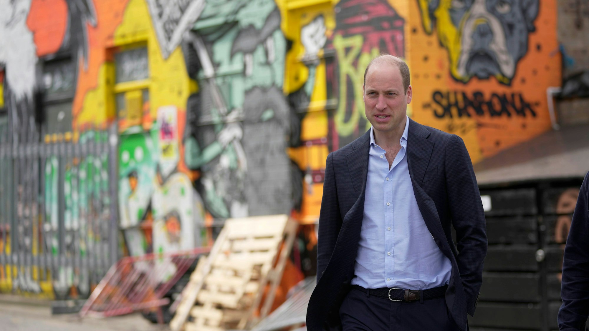 Prinz William steht vor einer Graffiti-Wand.