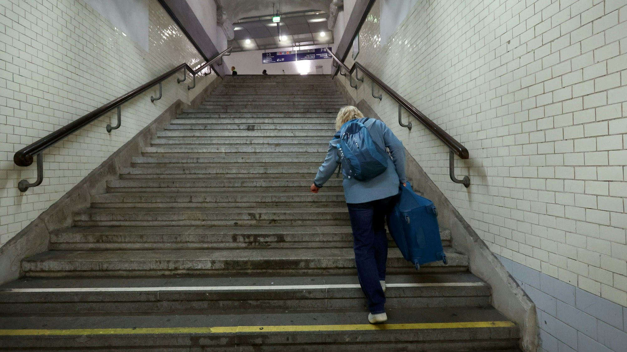Eine Frau schleppt einen Koffer im Kölner Bahnhof Messe/Deutz über eine steile Treppe.
