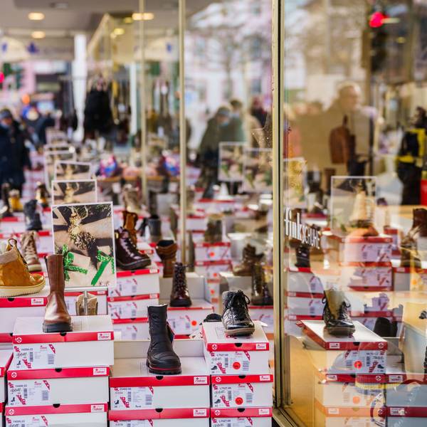 Menschen gehen an einem Schuhgeschäft in einer Innenstadt vorbei.