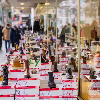 Menschen gehen an einem Schuhgeschäft in einer Innenstadt vorbei.