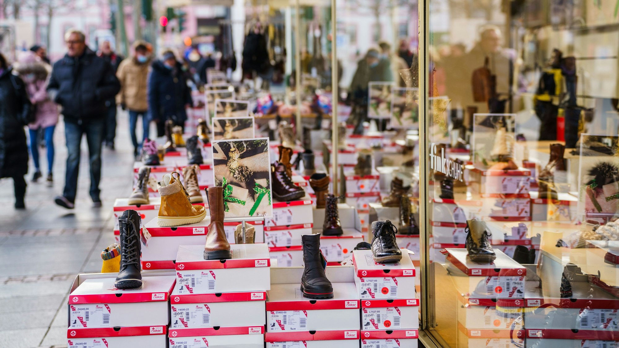 Menschen gehen an einem Schuhgeschäft in einer Innenstadt vorbei.