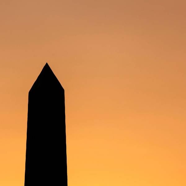 Die Spitze eines Obelisks steht schwarz vor einem orangefarbenen Himmel.