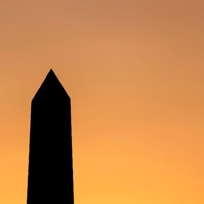 Die Spitze eines Obelisks steht schwarz vor einem orangefarbenen Himmel.