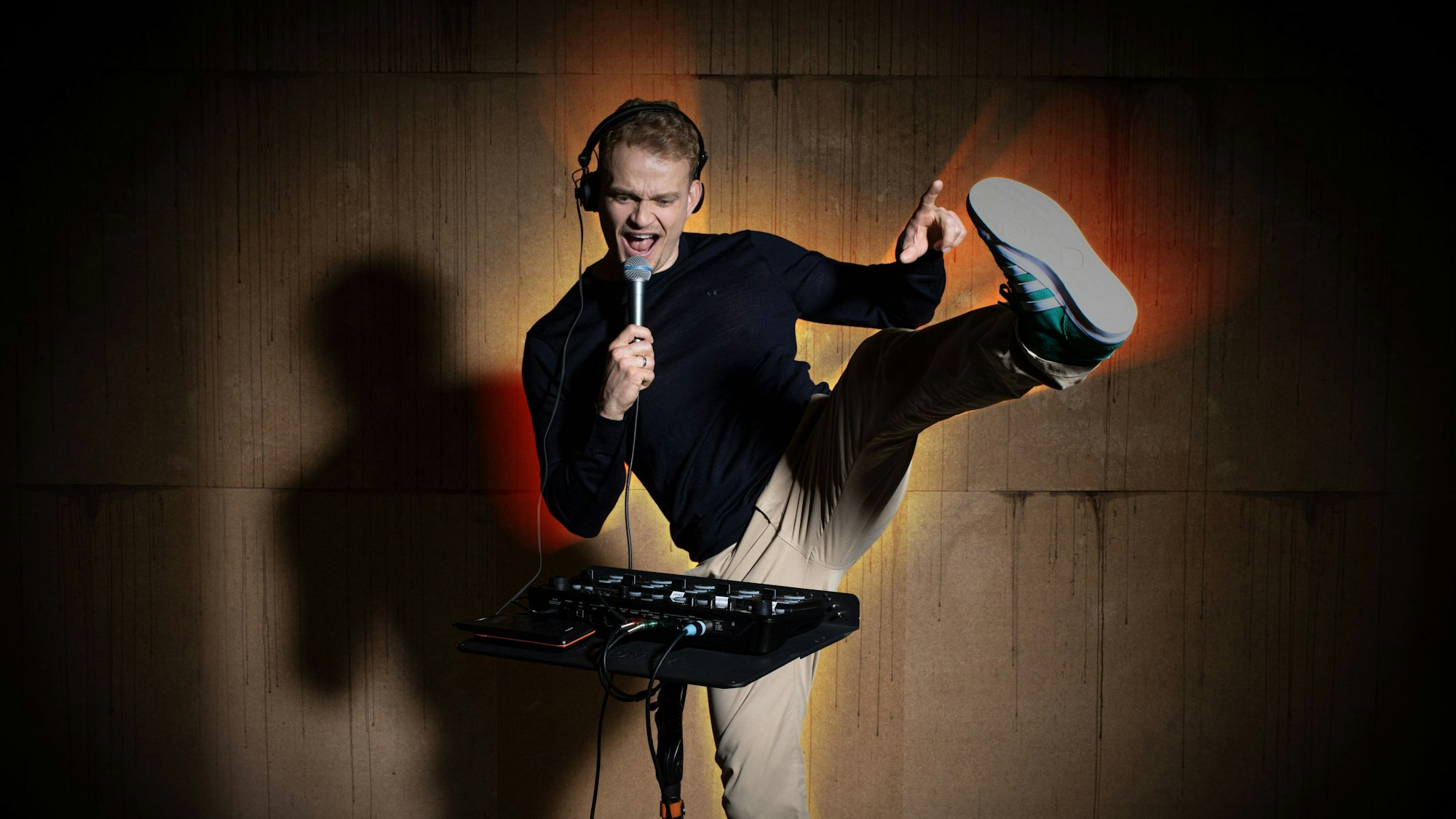 Das Bild zeigt den Künstler Dustin Waree hinter einem Mischpult. In der Hand hält er ein Mikrofon.