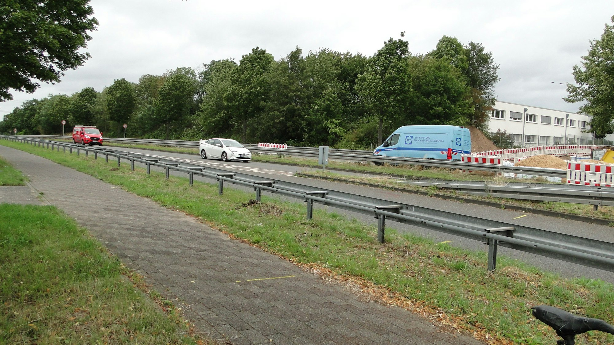 Autos fahren über eine Landstraße, ein Radweg ist durch Leitplanken abgetrennt.