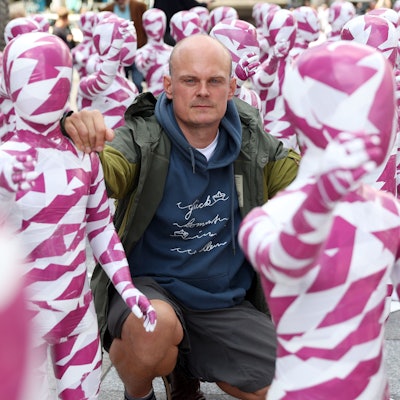 Dennis Josef Meseg
kniet zwischen weiß-purpur-farbigen Schaufensterpuppen.