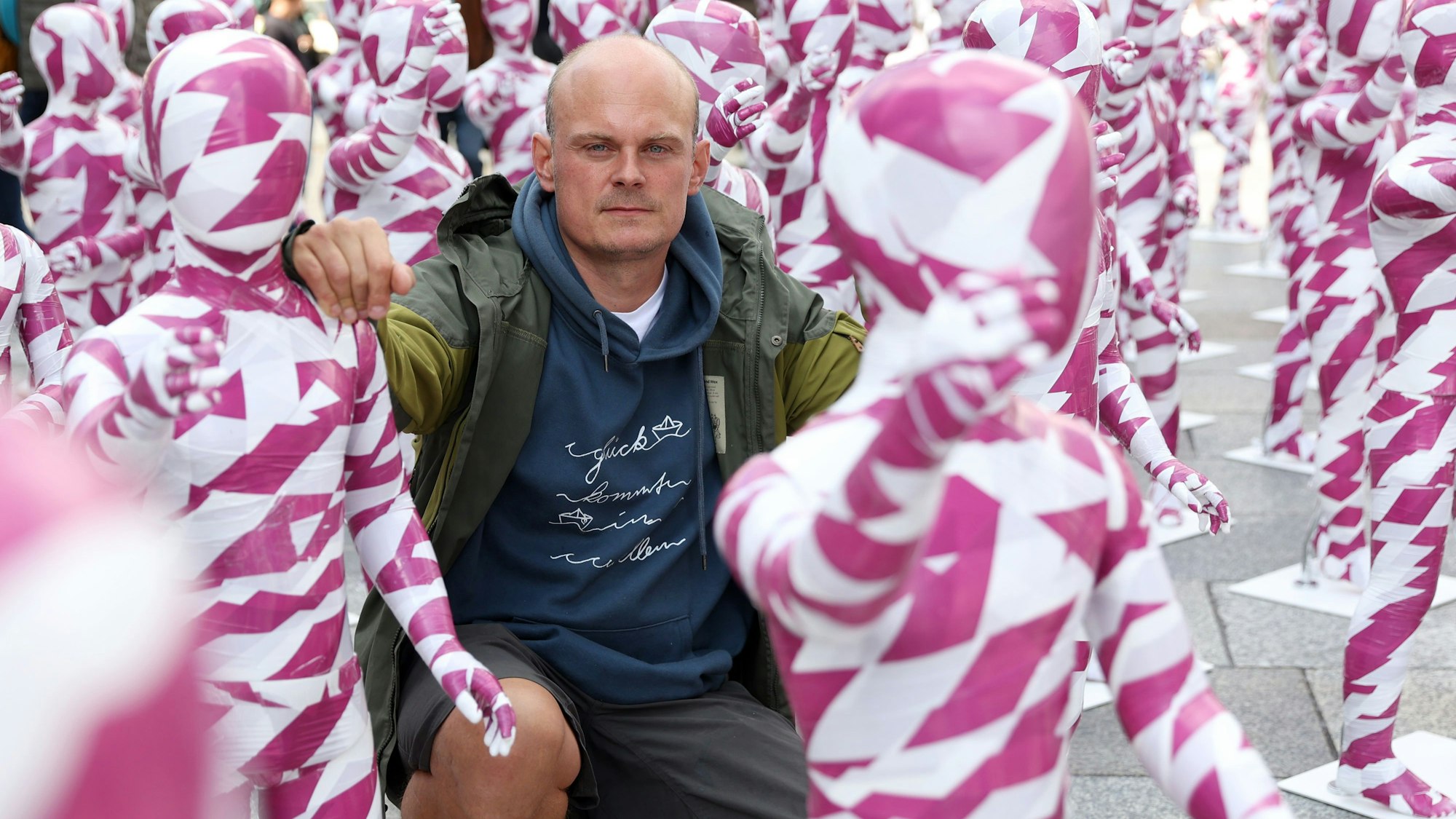Dennis Josef Meseg
kniet zwischen weiß-purpur-farbigen Schaufensterpuppen.