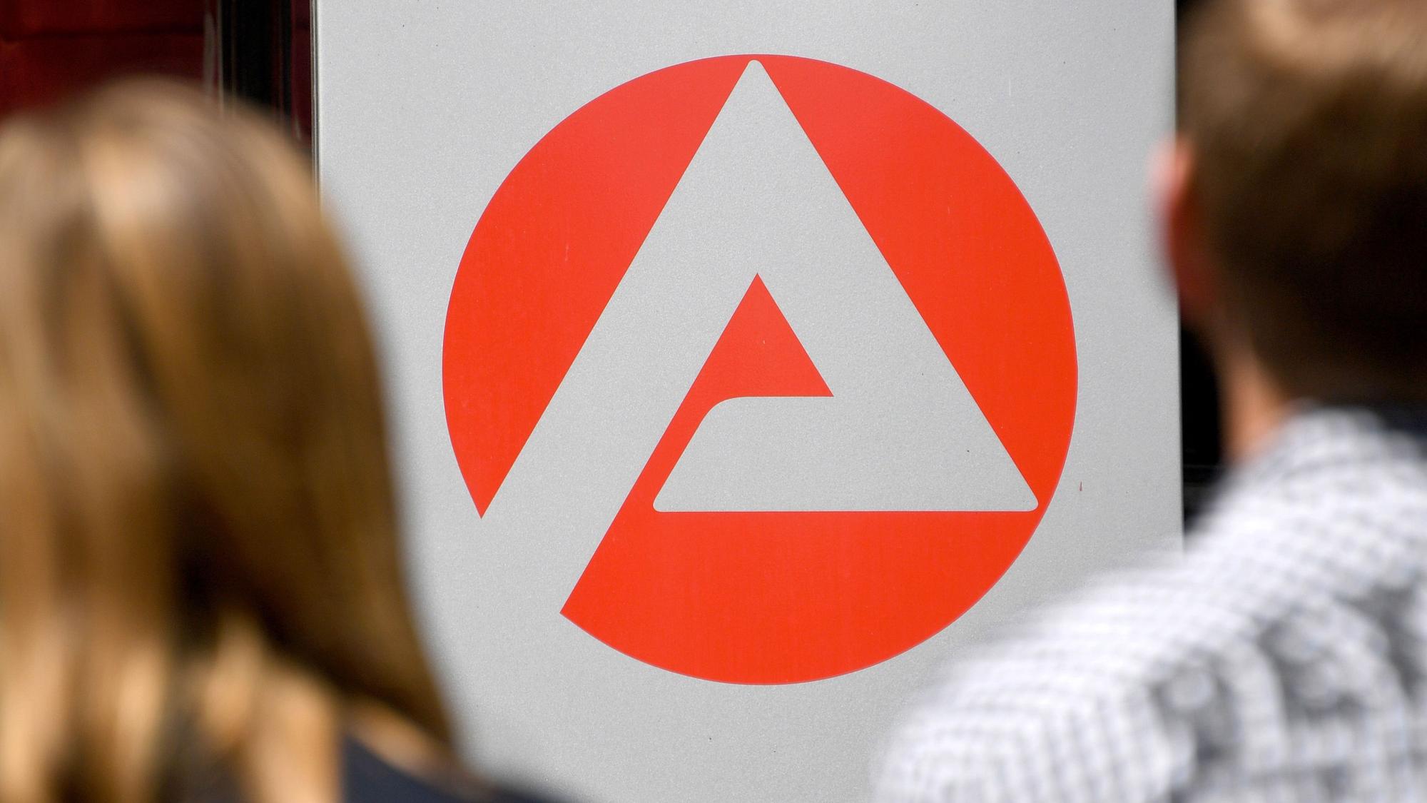 Zwei Personen stehen vor dem Logo der Agentur für Arbeit.