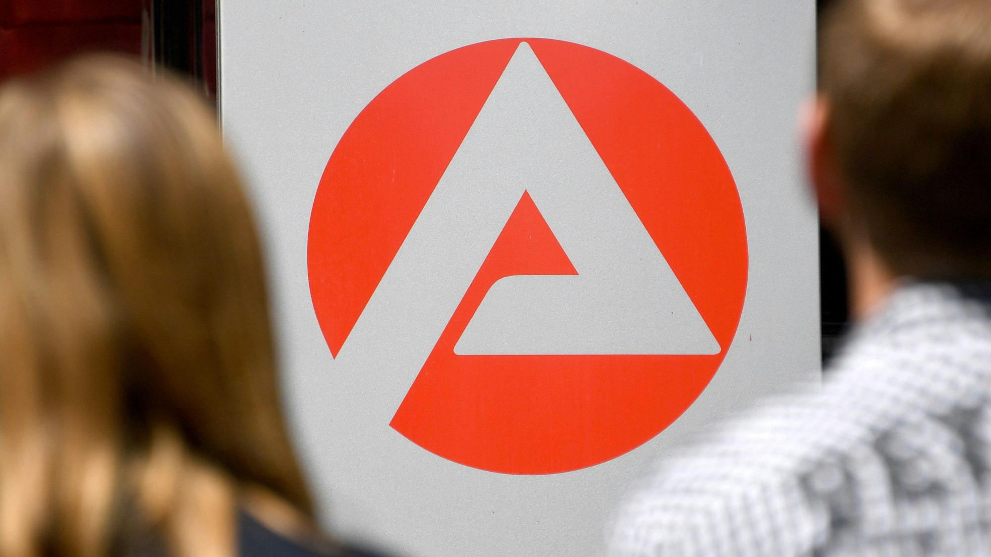 Zwei Personen stehen vor dem Logo der Agentur für Arbeit.