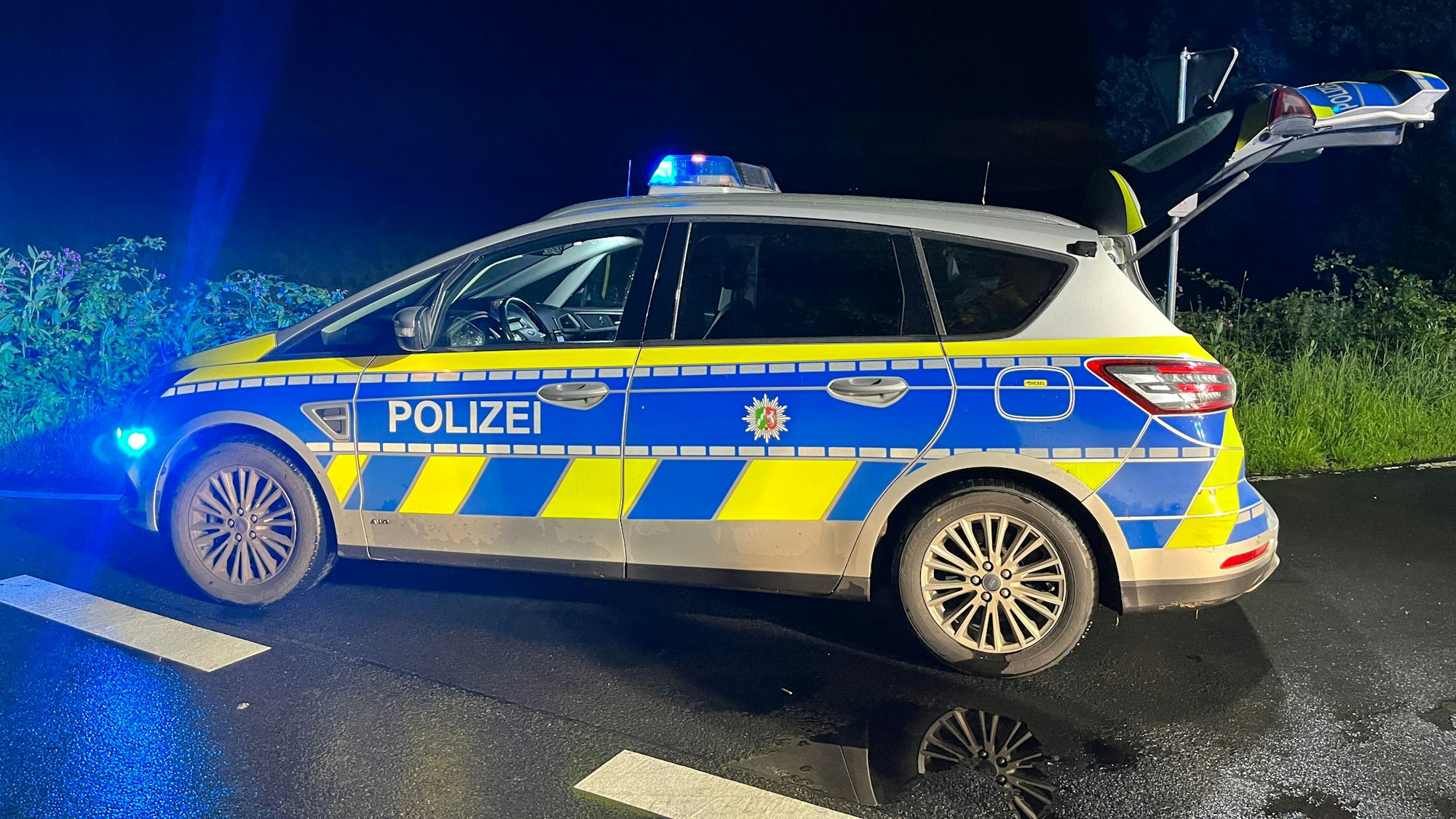Ein Streifenwagen steht mit eingeschaltetem Blaulicht bei Nacht an einer Kreuzung.