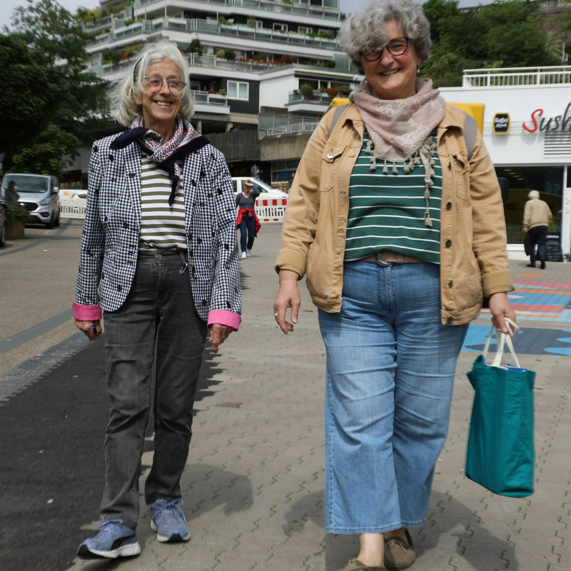 Zwei Frauen gehen mit Einkaufstasche die Bensberger Schloßstraße hinunter.