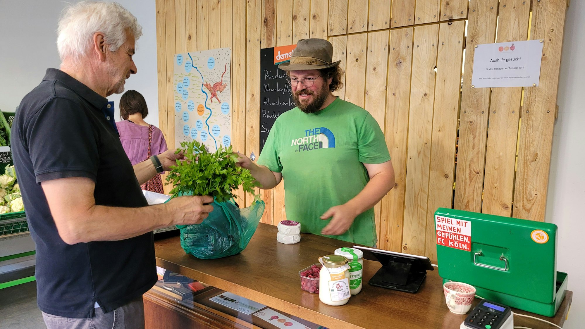 Das Foto zeigt den Landwirt, der sich an der Kasse mit einem Kunden unterhält.
