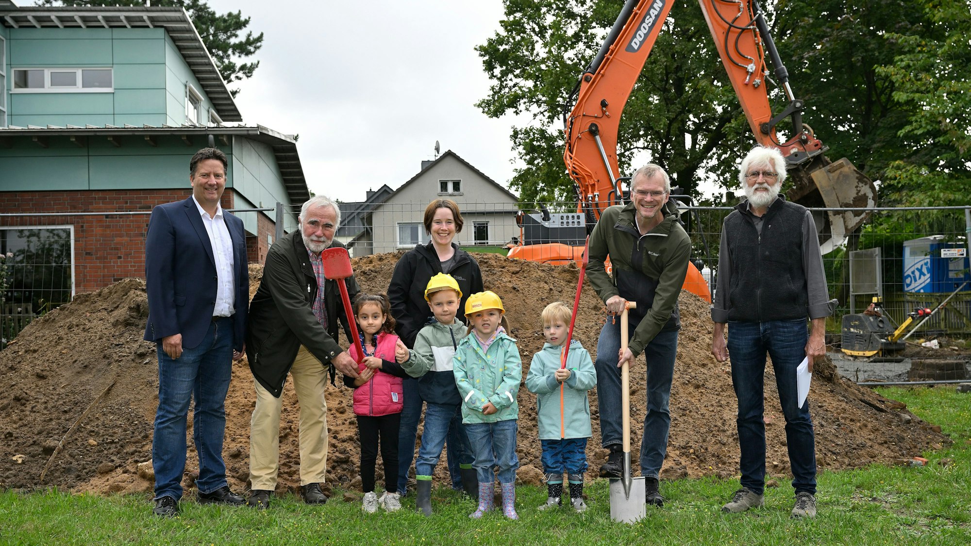 Beim Spatenstich für den Kita-Anbau der evangelischen Kirche Zum Frieden Gottes stehen Bürgermeister Frank Stein, Kita-Kinder und andere Beteiligte in einer Reihe.