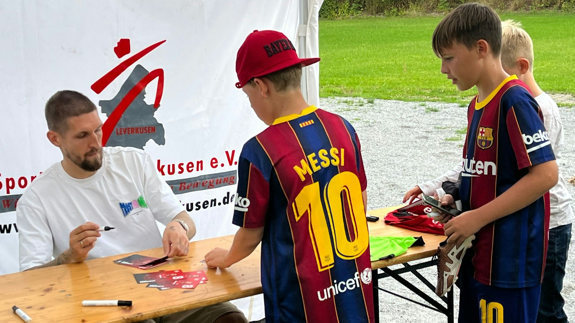 Bayer-04-Spieler Robert Andrich gibt Kindern am Rande der Fußballschule Autogramme.