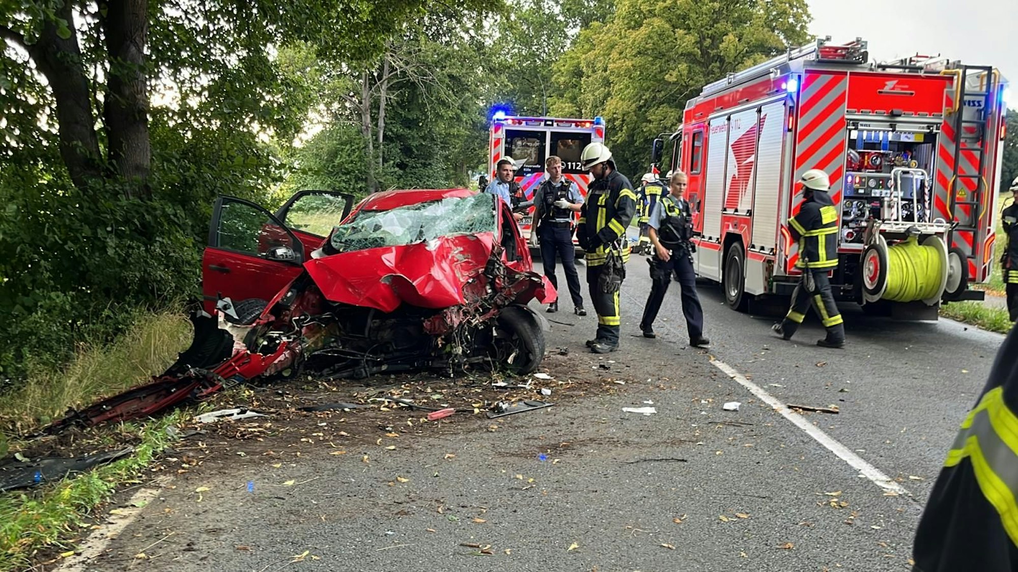 Schwerer Unfall in Köln-Worringen: Feuerwehrleute und Polizistinnen und Polizisten stehen am Dienstagbaend an dem extrem beschädigten Autowrack auf der Neusser Landstraße.