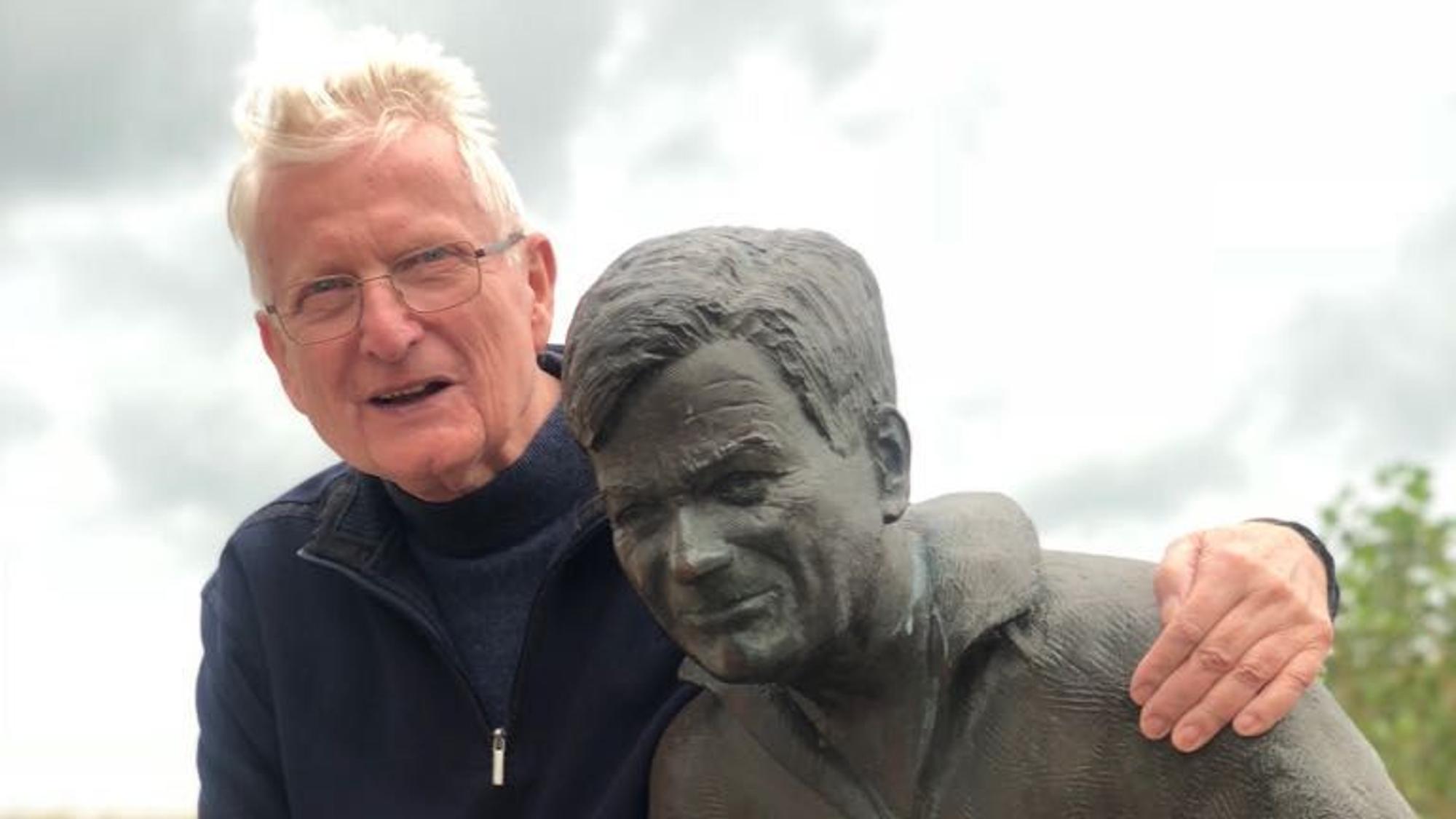 Franz Kersjes umarmt eine Statue und lächelt in die Kamera.